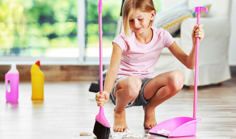 A Teenage girl collecting dirt in room with help of brush and dust pan