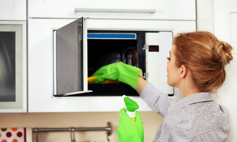 beautiful woman wiping a microwave