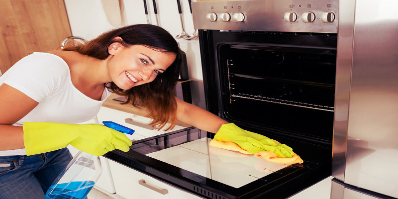 smiling girl wiping oven door glass