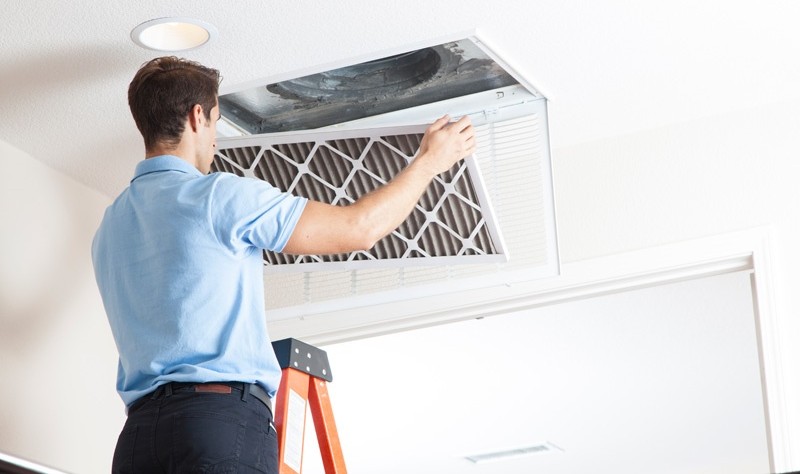 a young man is standing on a ladder and holding a air duct cover