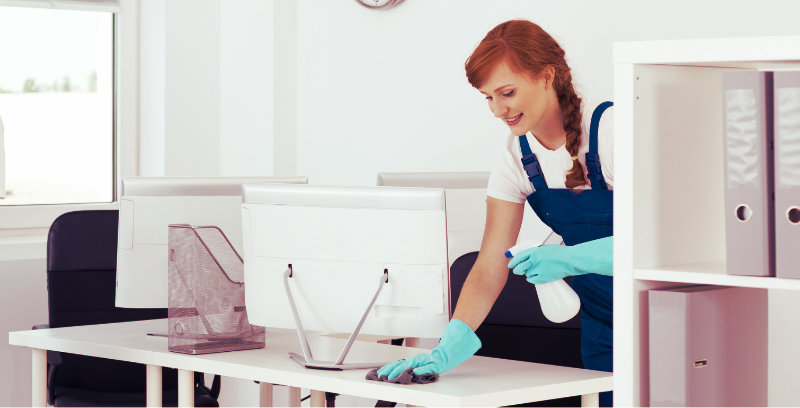 young woman wiping a desk with a cloth and disinfecting the surface