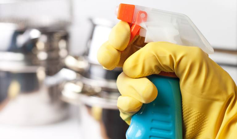 Hand of a woman in yellow gloves holding a bottle in her hand