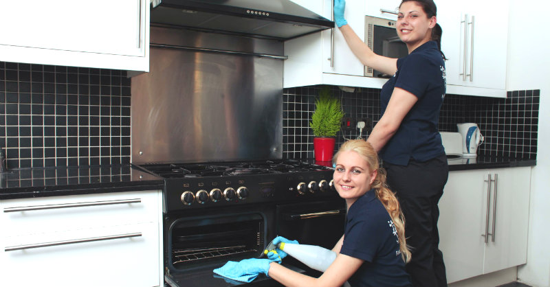 two women in black uniform wiping kitchen chimney and oven