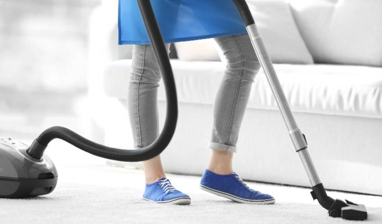 Woman is vacuuming her carpet inside her living room