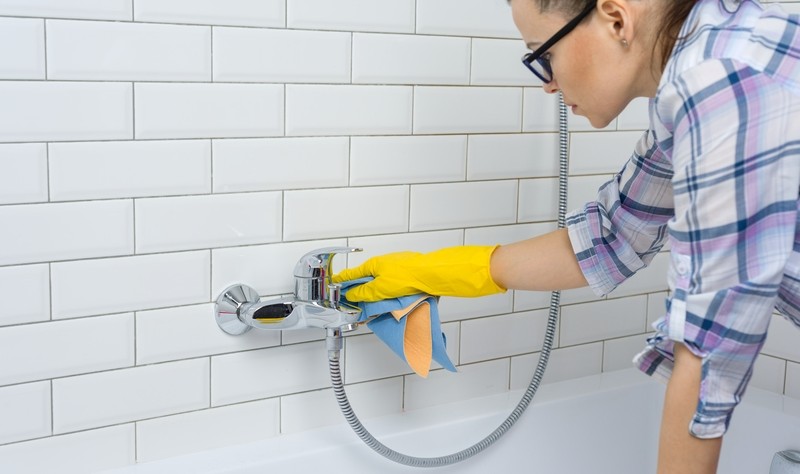 young woman wearing eye glasses wiping a shower jet with a cloth