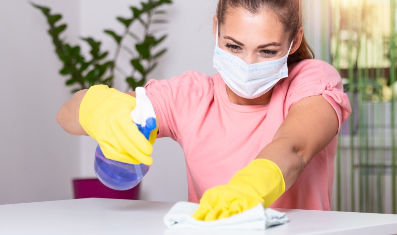 young woman wearing a mask disinfecting a surface