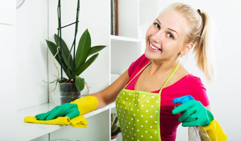 Woman in red top and yellow-green gloves scrubbing cabinet with yellow cloth.