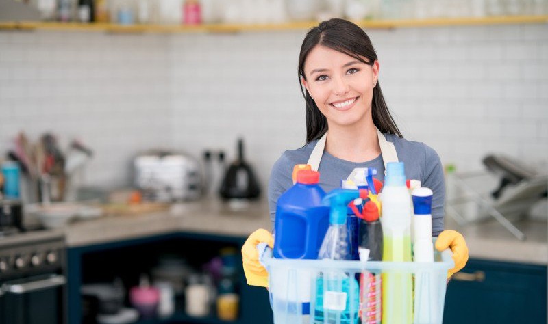 young woman holding a bucket full of chemical bottles and spray bottles