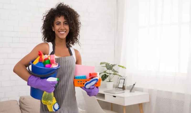 young woman holding a bucket full of spray bottles and brushes