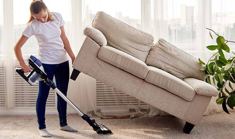 young woman vacuuming the hidden spaces inside of a house