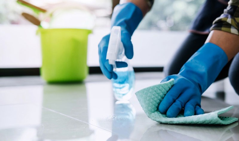 cropped picture of a woman with blue gloves wiping the floor