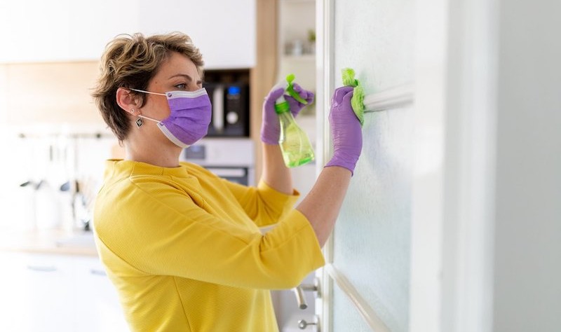 woman wearing a mask and gloves disinfecting a household surface