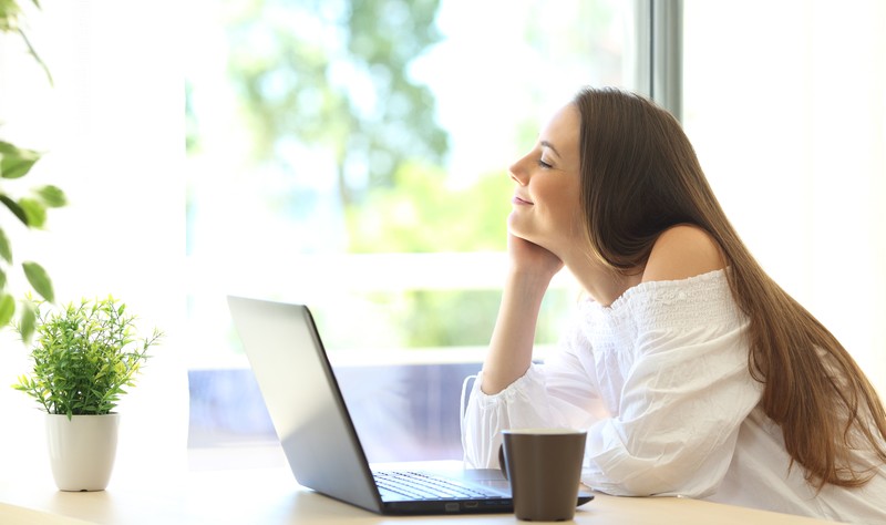 a happy woman sitting in her house with her laptop