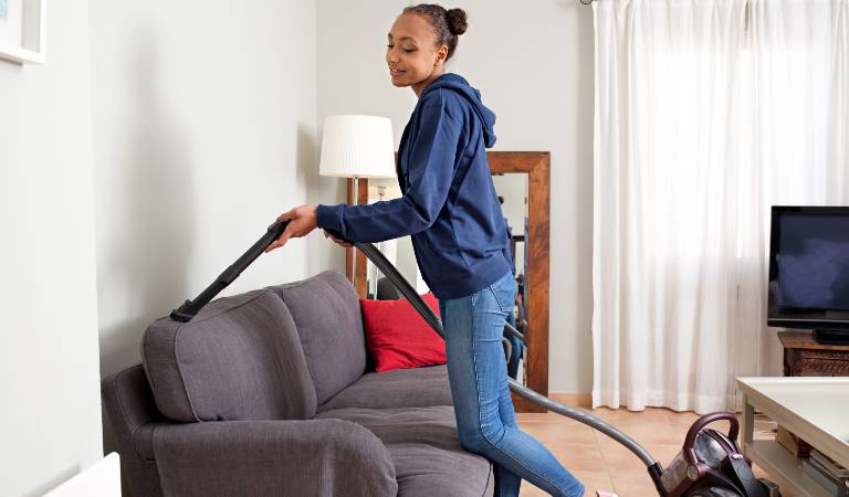 Woman is vacuuming her sofa inside a room