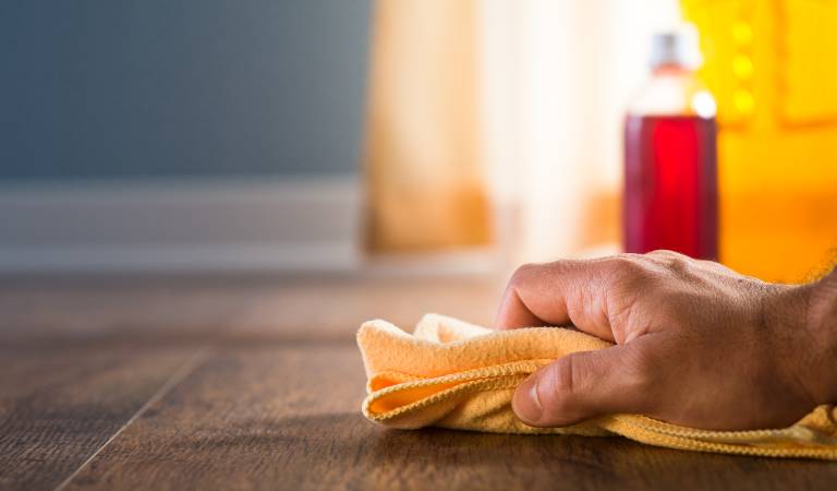 hand of a man scrubbing hardwood floor with cloth