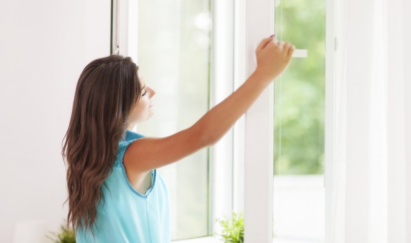 young woman opening a window and enjoying the fresh air