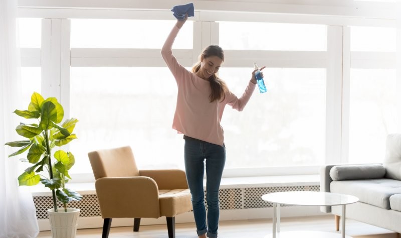 young happy woman dancing and holding a spray bottle and a cloth mop