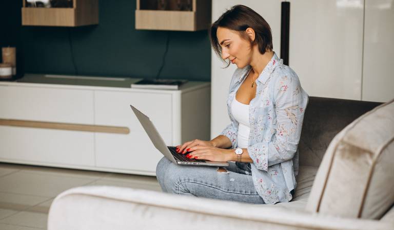 Woman sitting on sofa and working on her laptop