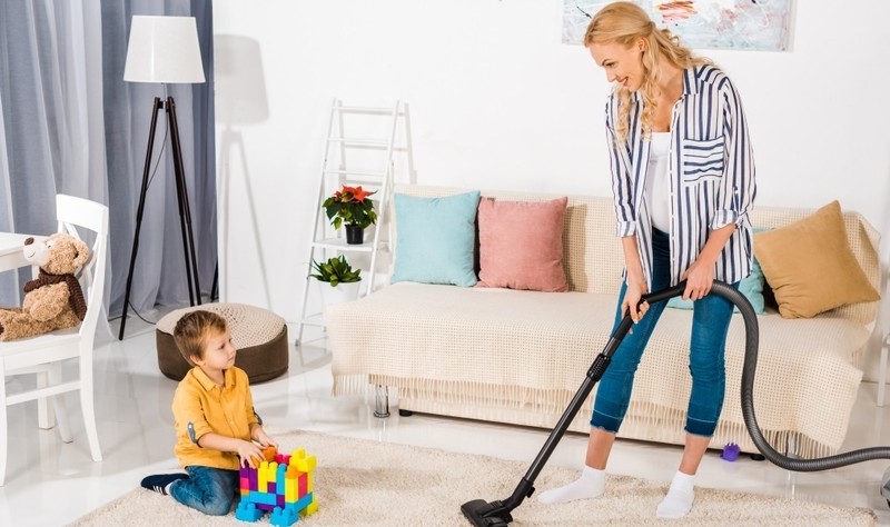 a beautiful young woman vacuuming a carpet and a kid is playing with toys