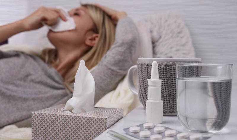 a sick woman laying on a bed and clearing her nose with a tissue