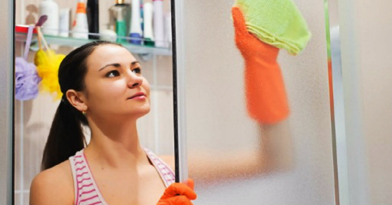 young beautiful woman wiping shower glass with rag
