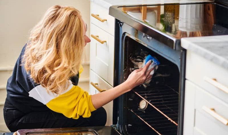 woman with blonde hair wiping an oven