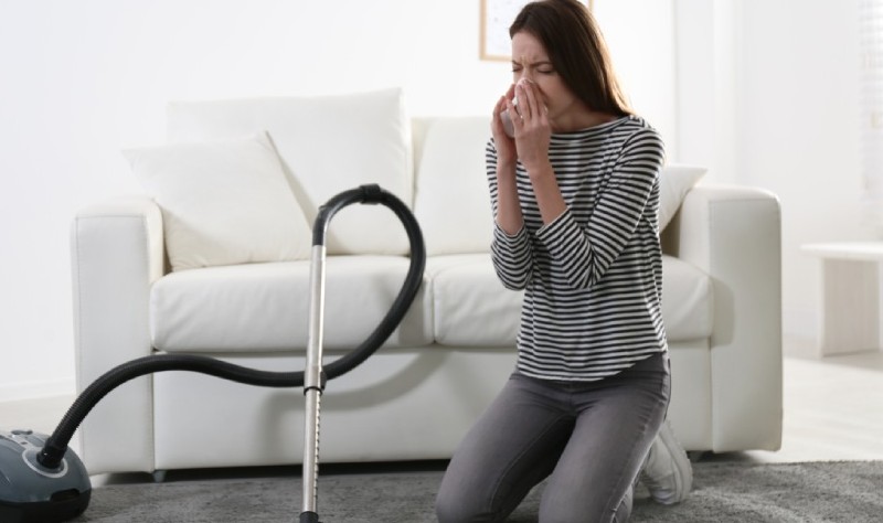young woman sneezing while vacuuming her house