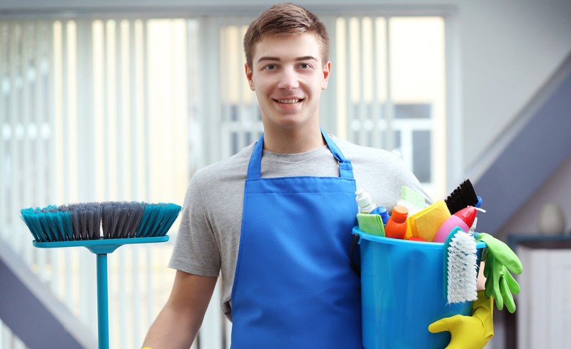 young professional holding a bucket full of spray bottles, brushes and gloves