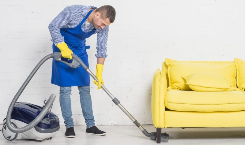 Young professional vacuuming a house with a vacuum cleaner