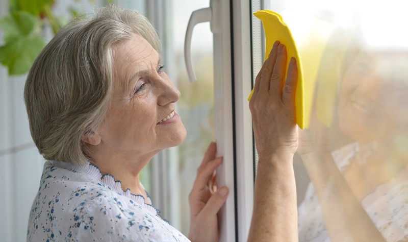 old age woman wiping a window glass with a cloth mop