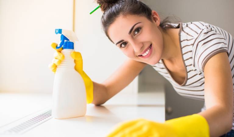 Woman in check top and yellow gloves holding a white bottle in her hand.