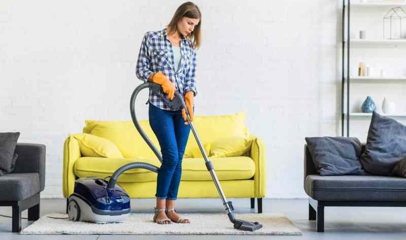 young woman vacuuming a carpet with a vacuum cleaner