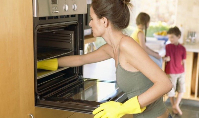 young woman wiping a oven with a cloth wipe