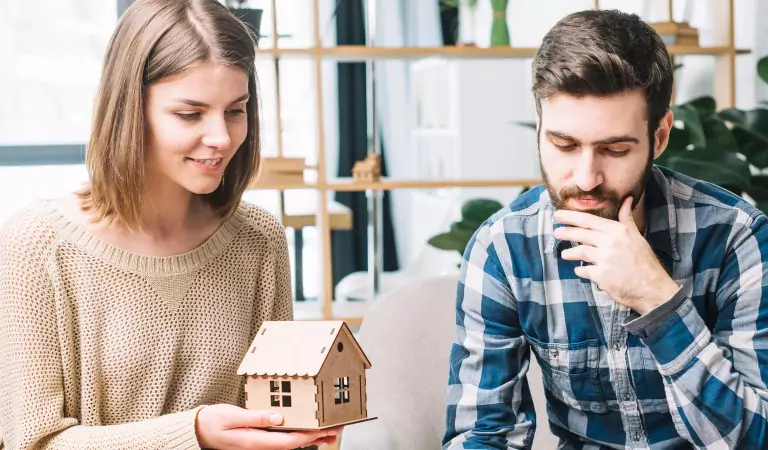 couple thinking about something and woman holding a dummy house in her hands