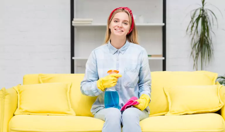 young woman sitting on a couch with some cleaning essentials