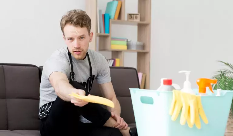 young man sitting inside of a house with a bucket full of cleaning supplies