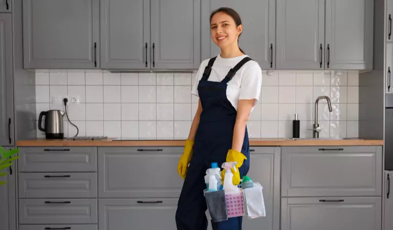 young professional cleaner holding a bucket full of cleaning supplies ready to clean her kitchen