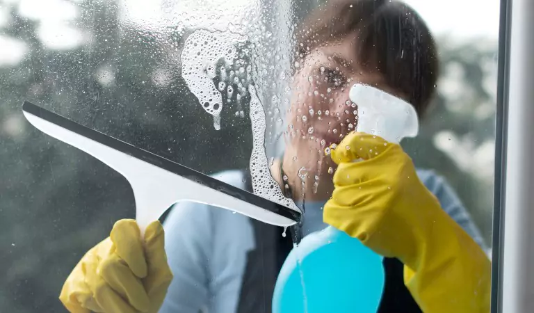 woman with a wiper and a cleaning spray cleaning a window glass
